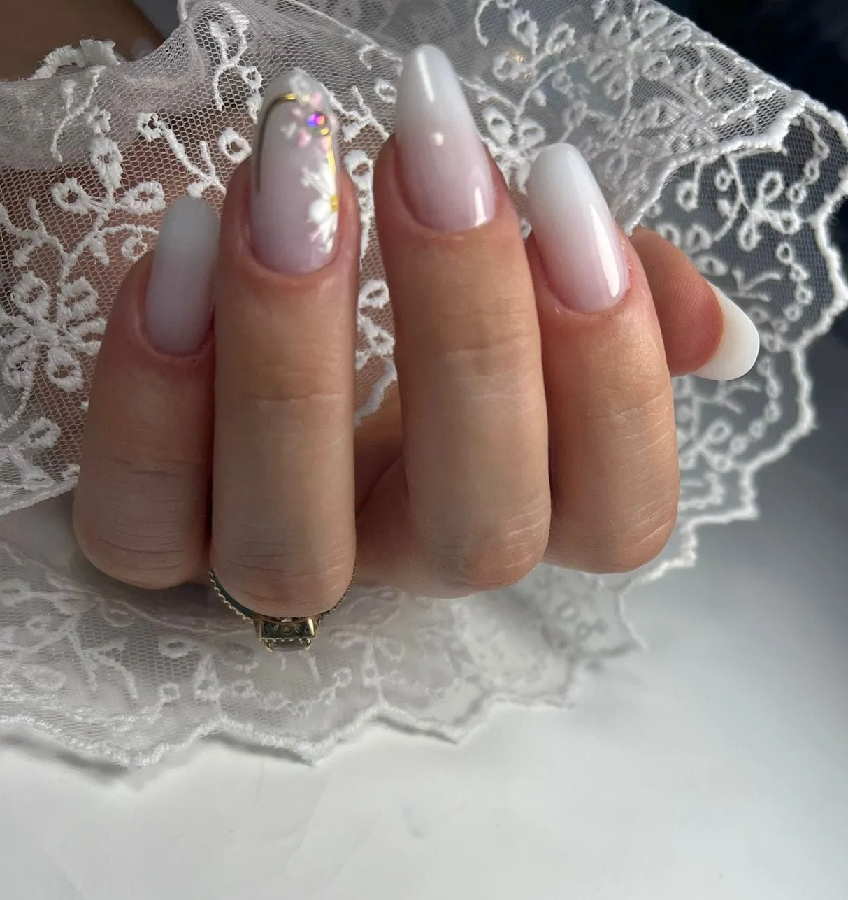 Manichiură ombré alb lăptos, formă migdală, cu floare și strasuri pe un deget